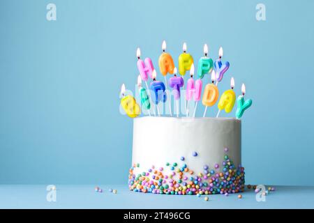 Bunte Geburtstagskuchen mit Geburtstagskerzen, die Happy Birthday auf blauem Hintergrund schreiben Stockfoto