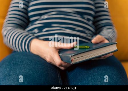 Eine nicht erkennbare Frau sitzt auf dem Sofa mit einem geschlossenen Notizbuch auf dem Schoß. Sie dachte, als sie auf dem Sofa saß. Einträge im Terminkalender. Einträge in einem Stockfoto