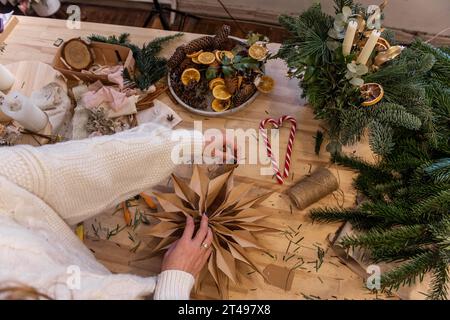 Das gesichtslose Mädchen ist justierender Stern aus Bastelpapier, das mit eigenen Händen auf Holztisch gemacht wurde. Natürliche Wohndekoration zu Weihnachten. Um die Sterne herum sind Kerzen Stockfoto