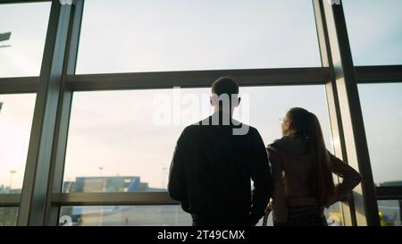 Attraktive junge Frau und ein hübscher Mann mit Koffern sind bereit für Reisen. In der Nähe von Panoramafenstern stehen, während Sie auf die Abfahrt warten. Ein Junge Stockfoto
