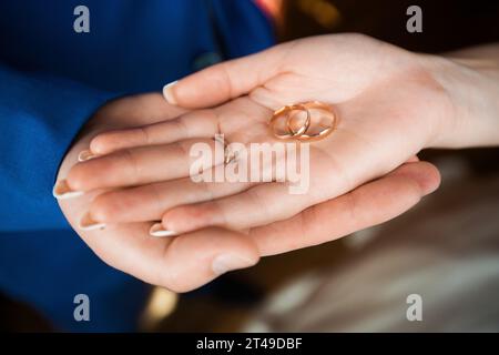 Nahaufnahme von Händen, die ineinander verwobene goldene Eheringe halten, die Engagement und ewige Liebe betonen. Stockfoto