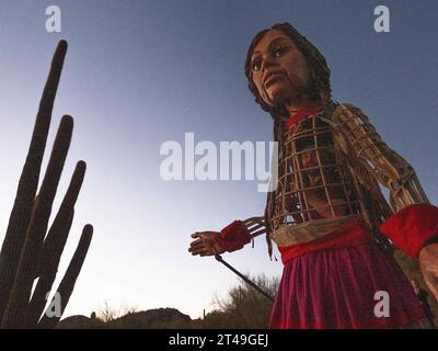 Tucson, Arizona, USA. Oktober 2023. Eine entschlossene kleine Amal, die 12 Fuß große Marionette eines 10-jährigen syrischen Flüchtlingsmädchens, macht sich bei Sonnenaufgang auf den Tumamoc Hill. Das Land ist heilig für einheimische indigene Stämme, die es vor mehr als 2000 Jahren besiedelten. Tumamoc ist Tohono O'Odham für die königliche Horneidechse, die Form des Berges. (Credit Image: © Sue Dorfman/ZUMA Press Wire) NUR REDAKTIONELLE VERWENDUNG! Nicht für kommerzielle ZWECKE! Stockfoto