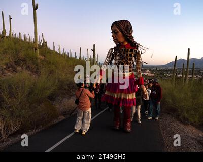 Tucson, Arizona, USA. Oktober 2023. Eine entschlossene kleine Amal, die 12 Fuß große Marionette eines 10-jährigen syrischen Flüchtlingsmädchens, macht sich bei Sonnenaufgang auf den Tumamoc Hill. Das Land ist heilig für einheimische indigene Stämme, die es vor mehr als 2000 Jahren besiedelten. Tumamoc ist Tohono O'Odham für die königliche Horneidechse, die Form des Berges. (Credit Image: © Sue Dorfman/ZUMA Press Wire) NUR REDAKTIONELLE VERWENDUNG! Nicht für kommerzielle ZWECKE! Stockfoto