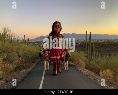 Tucson, Arizona, USA. Oktober 2023. Eine entschlossene kleine Amal, die 12 Fuß große Marionette eines 10-jährigen syrischen Flüchtlingsmädchens, macht sich bei Sonnenaufgang auf den Tumamoc Hill. Das Land ist heilig für einheimische indigene Stämme, die es vor mehr als 2000 Jahren besiedelten. Tumamoc ist Tohono O'Odham für die königliche Horneidechse, die Form des Berges. (Credit Image: © Sue Dorfman/ZUMA Press Wire) NUR REDAKTIONELLE VERWENDUNG! Nicht für kommerzielle ZWECKE! Stockfoto