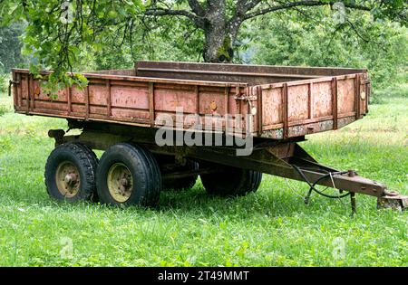 Ein alter, verlassener, rostiger Traktoranhänger. Auf dem Gras unter einem Apfelbaum stehen Stockfoto