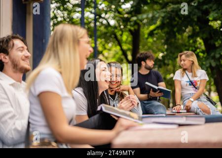 Glückliche Studenten, die Spaß während der Pause auf dem College-Hof haben, am Tisch sitzen Stockfoto