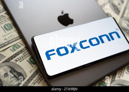 FOXCONN-Logo auf dem Smartphone, Apple-Logo auf dem iPad und US-Dollar-Scheine. Konzept. Stafford, Vereinigtes Königreich, 29. Oktober 2023 Stockfoto