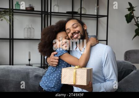 Friedlicher Daddy umarmt die kleine Tochter, die ein Überraschungsgeschenk hält Stockfoto