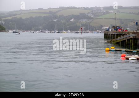 Blick auf East Portlemouth über die Salcome Mündung vom Hafen aus am nebeligen Sommertag, mit Bouys im Vordergrund und verankerten Booten in der Ferne Stockfoto