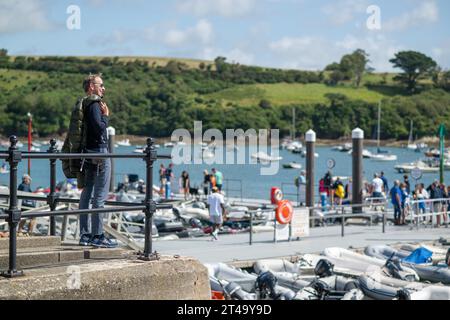 Mann, der in der Nähe eines Geländes steht, mit Jacke über der Schulter entspannt, Blick auf den Hafen von Salcombe und East Portlemouth, Snapes Point im Hintergrund Stockfoto