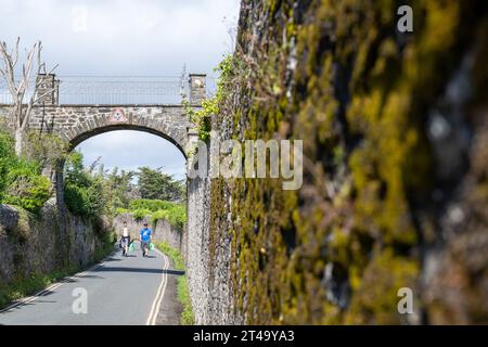 Blick auf die private Fußgängerbrücke über die Cliff Road, auf dem Weg nach North Sands, mit Menschen darunter und moosiger Mauer im Vordergrund. Stockfoto