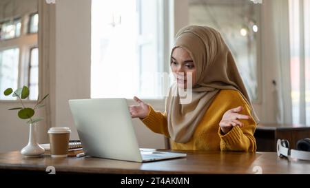 Eine professionelle und strenge asiatisch-muslimische Geschäftsfrau zuckt mit den Schultern und beschwert sich über ihren Mitarbeiter online über ein Online-Meeting, Feel Stockfoto