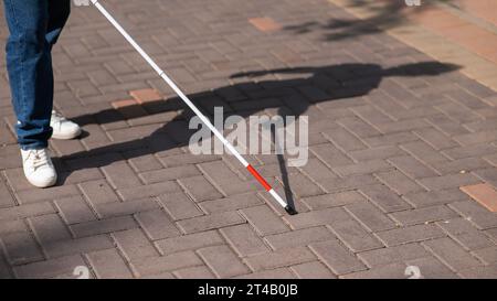 Eine gesichtslose blinde Frau läuft mit einem Stock die Straße entlang. Stockfoto