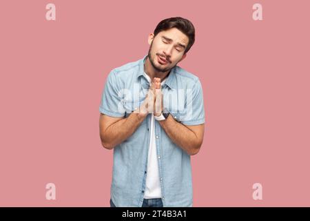 Hoffnungsvoller, trauriger bärtiger Mann, der um Vergebung bittet, Palmen in betender Geste hält, bittet um Gnade und sagt bitte, braucht deine Hilfe. Innenstudio, isoliert auf rosa Hintergrund. Stockfoto