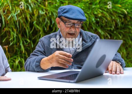 Pensionierter alter Mann mit Laptop in einem Garten eines Pflegeheims Stockfoto