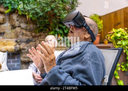 Älterer Mann, der eine Virtual-Reality-Brille benutzt, sitzt auf dem Garten einer Alten Stockfoto