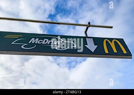 Schild in Höhe am Ständer mit Querstange mit weißer Schrift McDrive und gelbem Logo M von McDonald's über dem Eingang von Drive in zu Fast Food Stockfoto