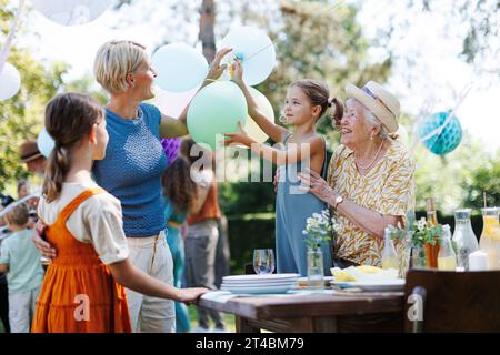 Großmutter, Mutter und Töchter, die Dekorationen für die Gartenparty im Sommer einrichten. Drei Generationen von Frauen in der Familie, die Teller, Essen und Getränke mitbringen Stockfoto