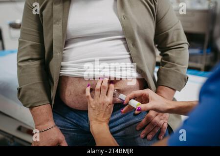 Der Arzt injiziert Insulin in den Bauch eines Patienten mit einem Insulinpen. Fettleibiger, übergewichtiger Mann besteht das Risiko, an Typ-2-Diabetes zu erkranken. Konzept von Stockfoto