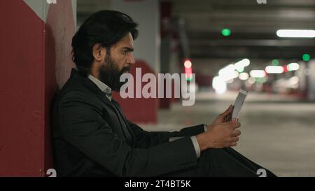 Besorgter, gestresster indischer Mann, der Laptop in der Tiefgarage benutzte und schlechte Nachrichten in sozialen Medien las, frustrierte traurige arbeitslose arabische Geschäftsleute, die aussahen Stockfoto