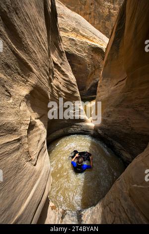 Mann schwimmt im Pool oder Schlagloch, während er den Wüstenschlucht, San Rafael Swell, Utah, absteigt. Stockfoto