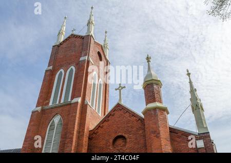 Eine nach oben geneigte Ansicht der Zwillings­türme der roten Backsteinkirche, blasse Pinakeln und Kreuze vor einem Himmel mit dünnen, cirrusartigen Wolken in Westfield, New York. Stockfoto