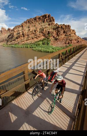 Zwei Biker fahren auf der Brücke, einer mit Kindertrager, Moab, Utah Stockfoto