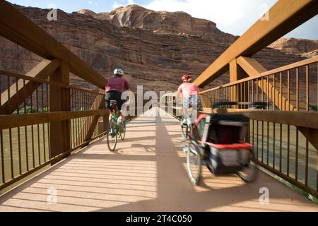 Zwei Biker auf der Brücke, einer mit Kindertragetasche Anhänger, Moab, Utah (unscharfe Bewegung) Stockfoto