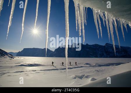Eiszyklen und Skifahrer durchqueren den gefrorenen Fjord nahe Baffin Island, Kanada Stockfoto