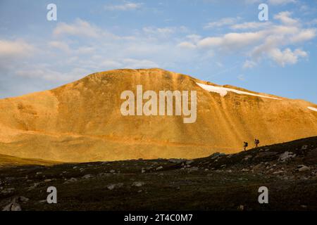 Zwei Personen, die bei Sonnenuntergang vor einem Berg wandern. Stockfoto