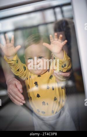 Porträt eines süßen lächelnden Jungen, der durch das Fenster schaut. Freude und Glück Konzept. Liebe und familiäre Emotionen Stockfoto