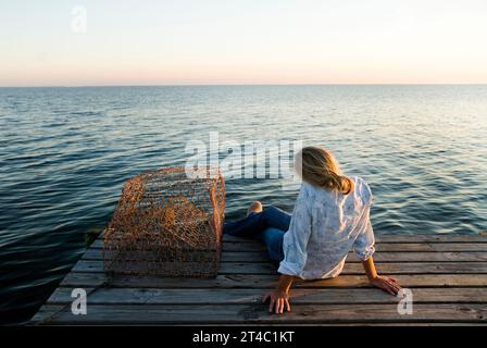 Eine junge Frau ruht bequem auf einem Dock mit Blick auf die ruhigen Gewässer des Golfs von Mexiko. Stockfoto
