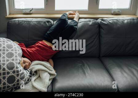 Der gelangweilte Junge liegt mit dem Kopf auf der Rückseite der Couch Stockfoto