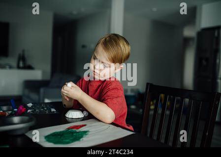 Der kleine Junge schaut ernsthaft auf die Hände, während er an einer Rechnung bastelt Stockfoto