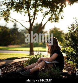 Kleines Mädchen, das im Frühling draußen Hausaufgaben macht Stockfoto