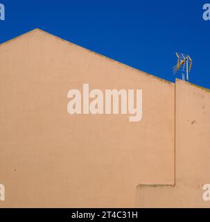Gelb-ockerfarbene Hauswand mit Satellitenantenne vor einem blauen Himmel - Griechenland Stockfoto
