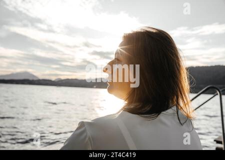 Eine Frau in gelbem Kleid sitzt auf einem Damm am See bei Sonnenuntergang Stockfoto
