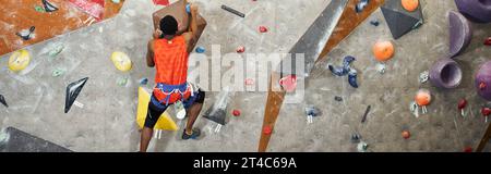 Rückansicht eines athletischen afroamerikanischen männlichen Modells mit alpinem Gurtzeug, das auf eine Felswand klettert, Banner Stockfoto