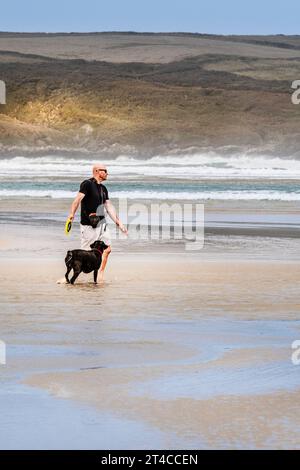 Ein Mann, der mit seinem Hund am Crantock Beach in Newquay in Cornwall spielt. Stockfoto