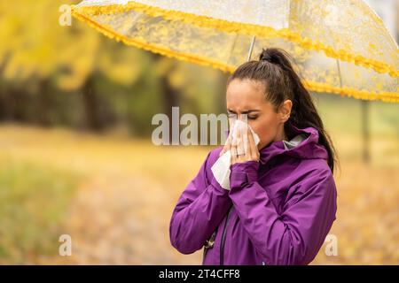 Eine Frau, die sich die Nase bläst und an einem regnerischen Herbsttag in ein Taschentuch niest. Stockfoto