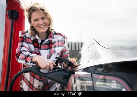 Eine Frau in einem karierten Hemd lädt ein Elektroauto auf. Stockfoto