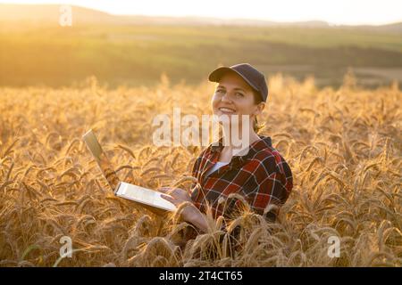 Eine Farmerin, die mit einem Laptop auf einem Weizenfeld arbeitet. Intelligente Landwirtschaft und digitale Landwirtschaft. Stockfoto