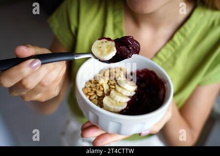 Acai-Schüssel. Nicht identifizierte Frau, die einen brasilianischen Acai mit Banane und Müsli zum Frühstück zeigt. Stockfoto