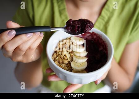 Junge Frau isst brasilianisches Acai aus einer Schüssel mit Banane und Müsli zum Frühstück Stockfoto