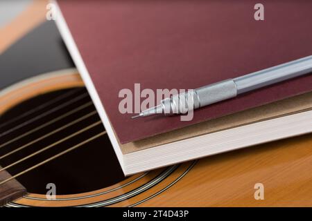 Bleistift und Notizbuch auf Akustikgitarre. Stockfoto