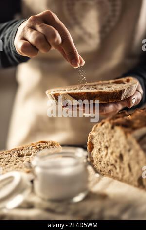 Weibliche Köchin salzt eine frische Scheibe Brot - Nahaufnahme. Stockfoto