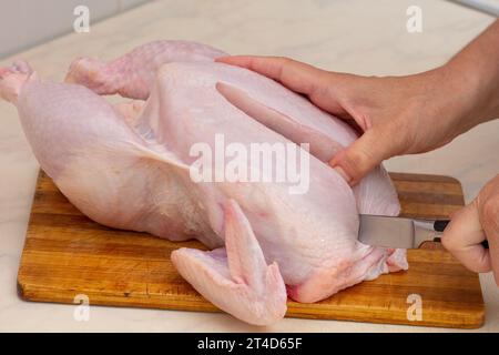 Frau, die ganze rohe Hühner auf hölzernem Schneidebrett von Hand schneidet Stockfoto
