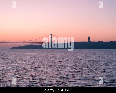 Ein Blick auf den Sonnenaufgang auf die Brücke 25 de Abril in Lissabon, Portugal. Schuss aus öffentlichem Grundstück neben dem Belem Tower Stockfoto