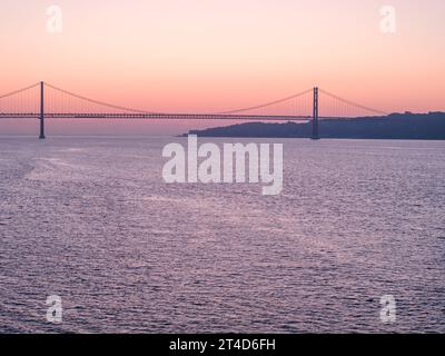 Ein Blick auf den Sonnenaufgang auf die Brücke 25 de Abril in Lissabon, Portugal. Schuss aus öffentlichem Grundstück neben dem Belem Tower Stockfoto