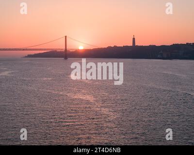 Ein Blick auf den Sonnenaufgang auf die Brücke 25 de Abril in Lissabon, Portugal. Schuss aus öffentlichem Grundstück neben dem Belem Tower Stockfoto